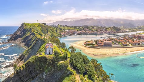 Aerial panorama of a church on top of the cliffs with views of the beach and mountains in Principality of Asturias, Spain.