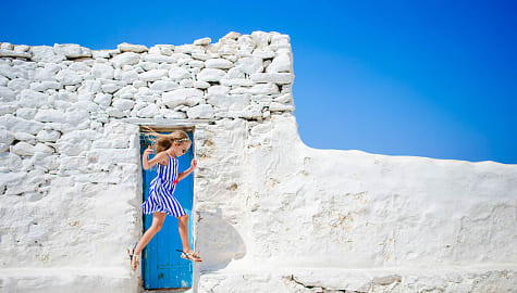 Young daughter jumping in front of blue door on Mykonos Island, Greece