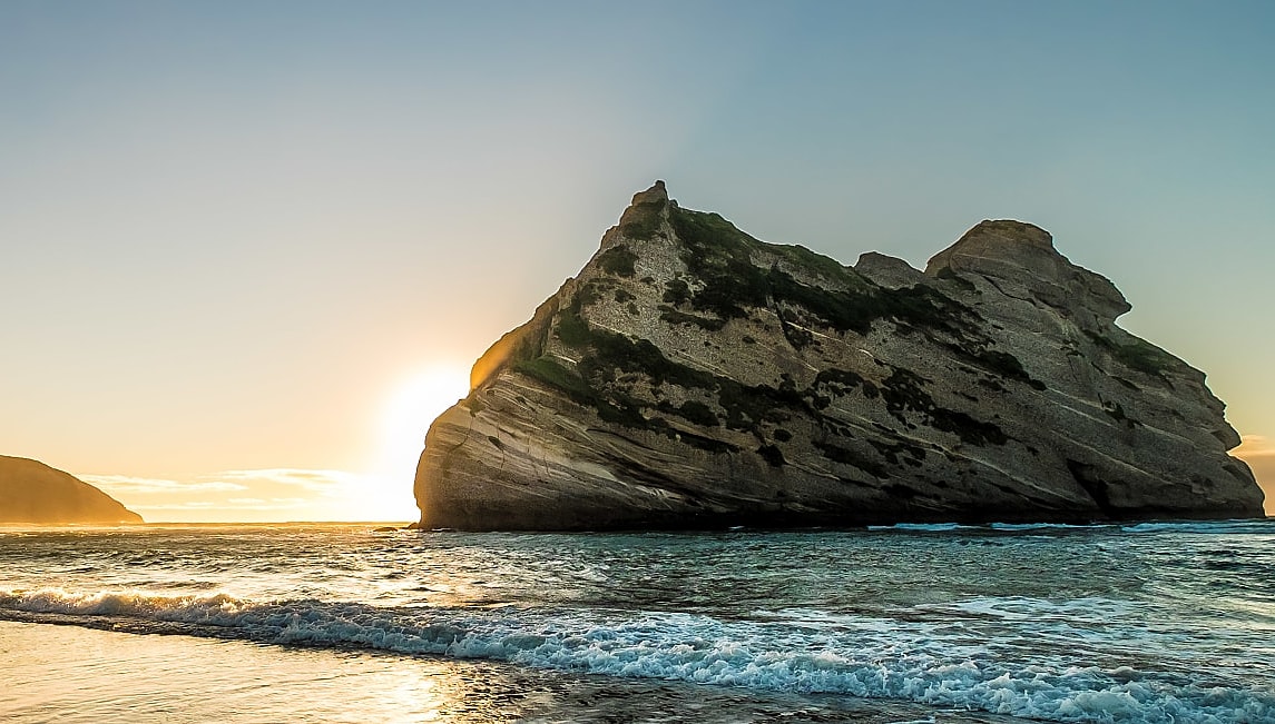 Sun rising behind the rock formation at Wharariki Beach on the South Island of New Zealand.
