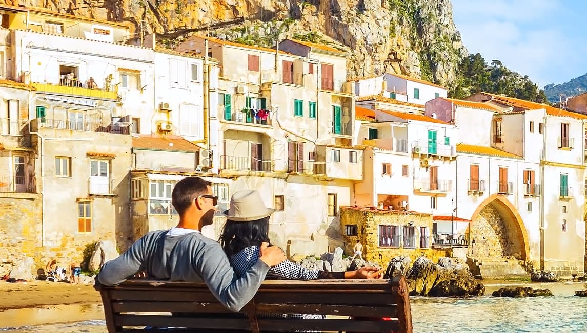 Couple on bench looking at colorful houses in Sicily, Italy
