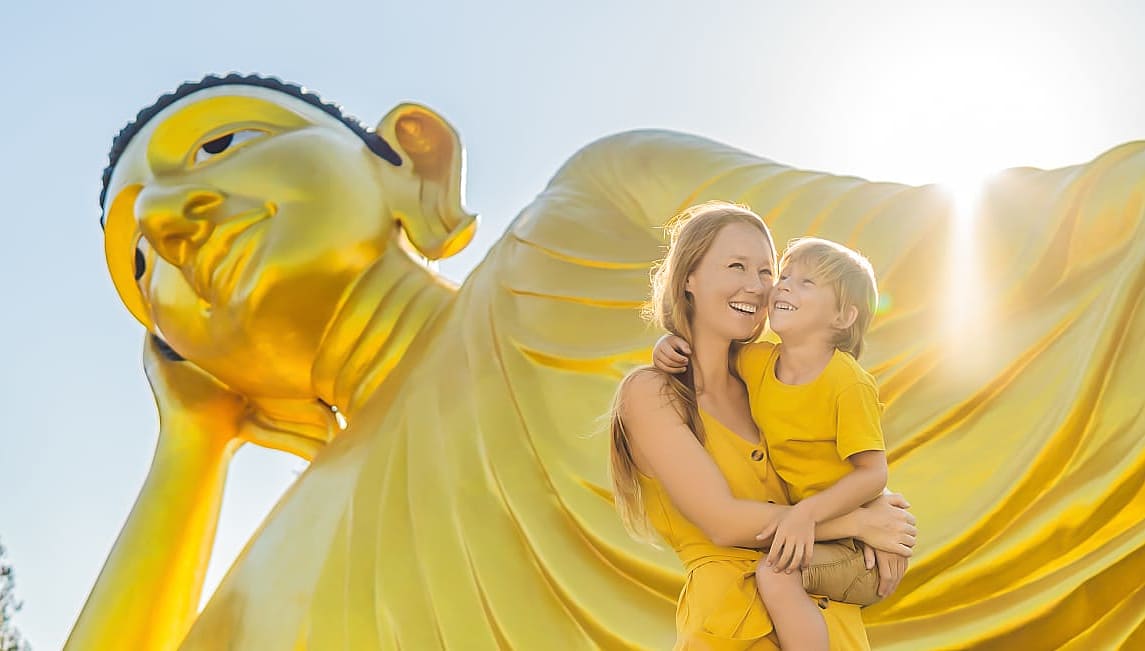 Mother and son on vacation pose in front of Lying Buddha statue in Thailand.