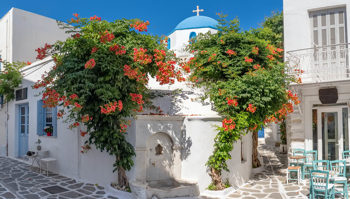 Narrow street in Greece with cozy outdoor cafe and traditional greek church in Parikia village on Paros island, Cyclades.