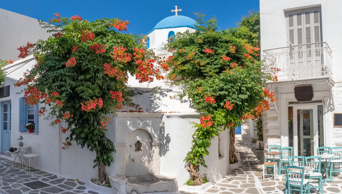 Narrow street in Greece with cozy outdoor cafe and traditional greek church in Parikia village on Paros island, Cyclades.