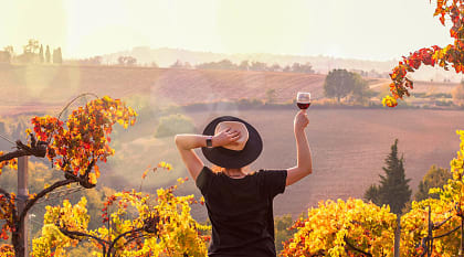 Woman raising a glass of wine, enjoying the view at sunset in Tuscany