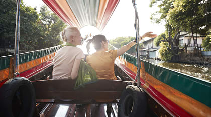 Senior travelers riding a colorful longtail boat through a canal at sunset in Bangkok, Thailand