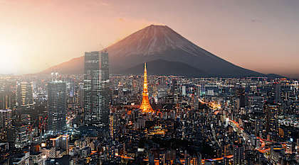 The Tokyo skyline at sunset, featuring the silhouette of Mount Fuji behind the glowing orange frame of the Tokyo Tower.