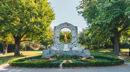 Golden Johann Strauss statue in Stadtpark, Vienna, surrounded by trees and a beautiful garden setting