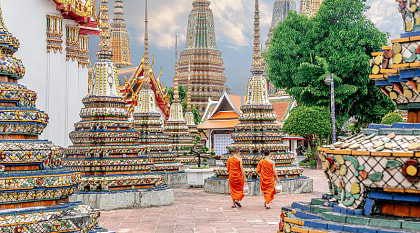 Two monks in colorful orange robes walking through Wat Pho Temple in Bangkok, Thailand