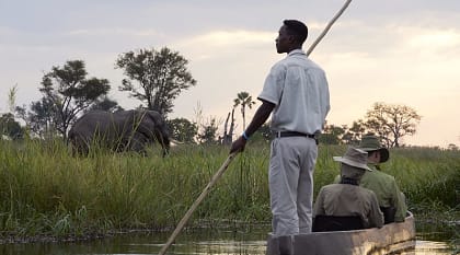 Mokoro boat on the Okavango Delta in Botswana Mokoro boat safari with elephant on riverbank at Sanctuary Baines Camp in Botswana