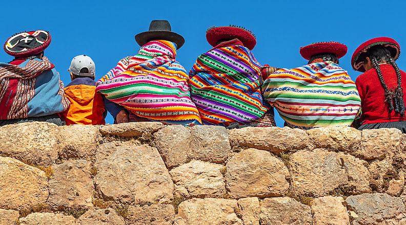 Cusco, Peru Native Peruvian women pose on a rock wall with a young tourist in Cusco