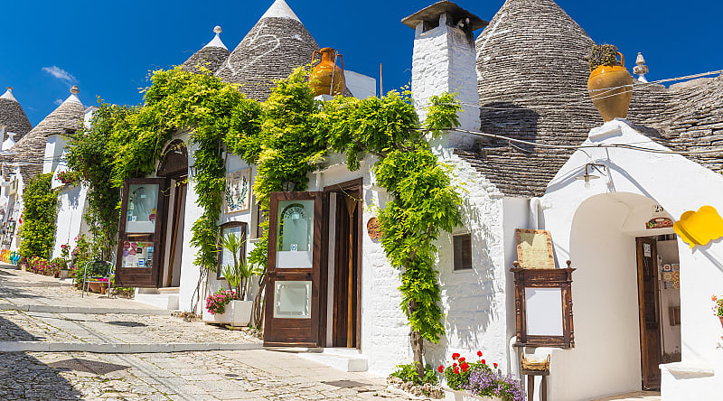 Beautiful town of Alberobello with trulli houses among green plants and flowers in the Apulia region of southern Italy. Beautiful town of Alberobello with trulli houses among green plants and flowers in the Apulia region of southern Italy.