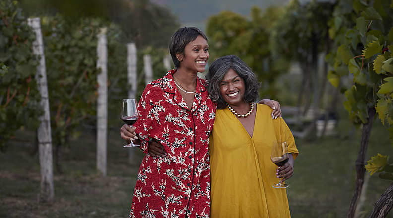 Smiling mother and daughter holding wineglasses and standing with arms around each other at a vineyard