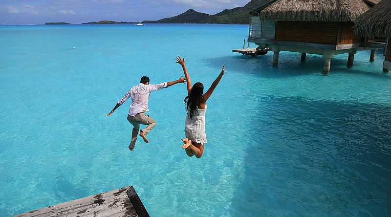 Happy young couple jump into the water from their over water bungalow in Bora Bora