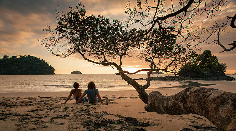 Manuel Antonio, Costa Rica Couple sitting on the beach watching the sunset in Manuel Antonio National Park