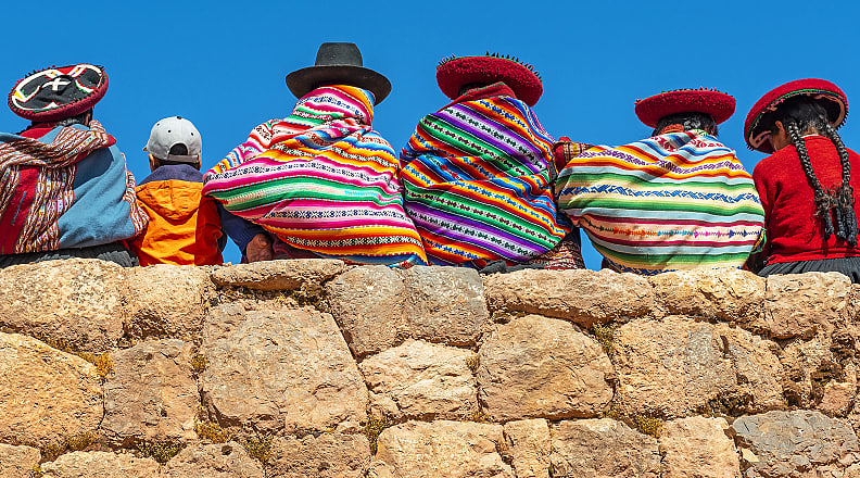 Cusco, Peru Native Peruvian women pose on a rock wall with a young tourist in Cusco