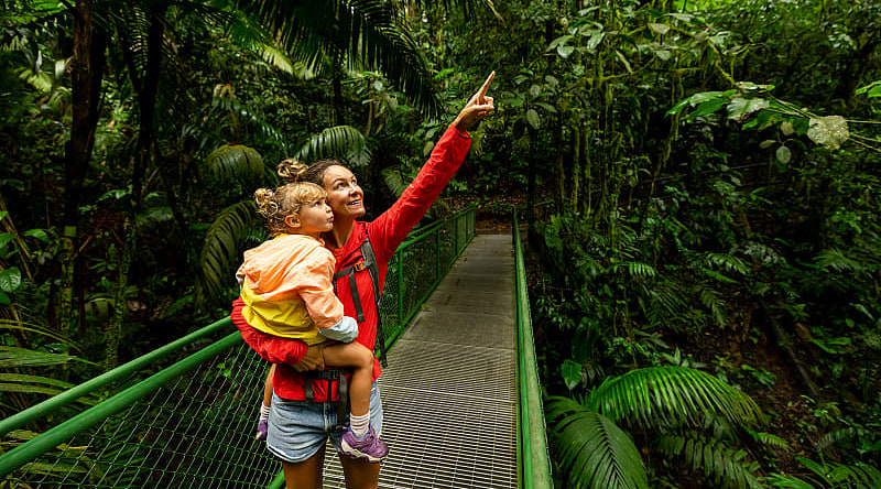 Classic Family Costa Rica Vacation "Mother and child on a rainforest walkway in Arenal, Costa Rica, exploring and pointing at the lush greenery.