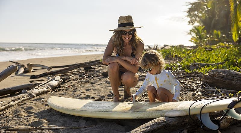 A young girl learning how to wax a surf board from her mother in Costa Rica