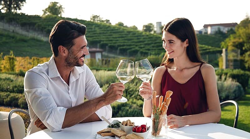 Happy couple enjoying romantic dinner with wine at a vineyard in Italy