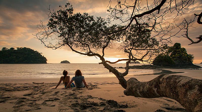 Couple sitting on the beach watching the sunset in Manuel Antonio National Park