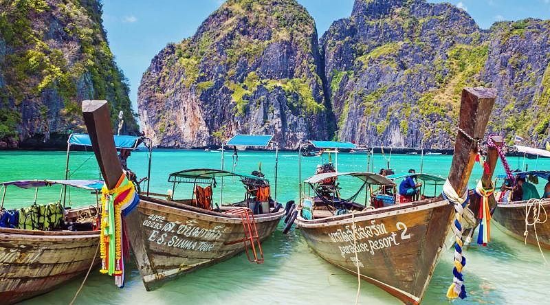 Wooden boats in the turquoise waters of Maya Bay with limestone karst cliffs on Phi Phi island in Thailand Wooden boats in the turquoise waters of Maya Bay with limestone karst cliffs on Phi Phi island in Thailand