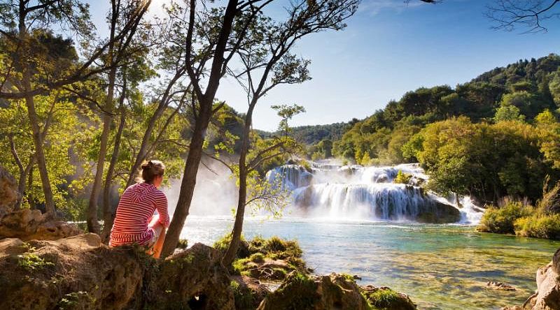 Croatia Tour for Seniors: Sophistication and Adventure Woman traveler relaxing and viewing the waterfalls in Krka National Park, Croatia