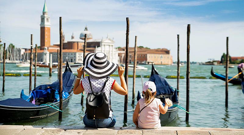 Mother and daughter sitting in front of gondolas looking at San Giorgio Maggiore in Venice, Italy