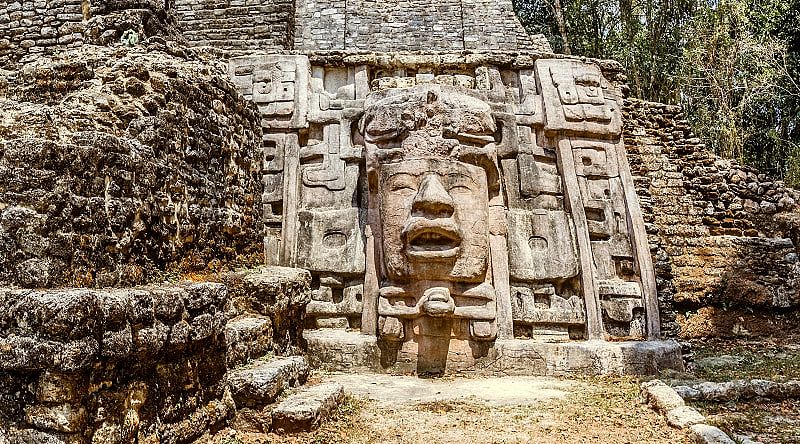 Ancient stone Mayan pre-columbian civilization pyramid with carved face in the forest, Lamanai archeological site, Orange Walk District, Belize Ancient stone Mayan pre-columbian civilization pyramid with carved face in the forest, Lamanai archeological site, Orange Walk District, Belize