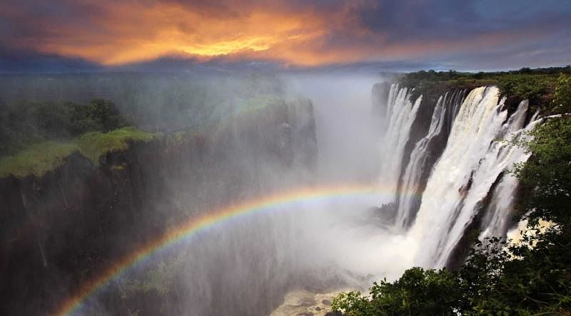 Gorgeous view of Victoria Falls at sunset with a rainbow forming in the mist, Zambia, Africa Gorgeous view of Victoria Falls at sunset with a rainbow forming in the mist, Zambia, Africa