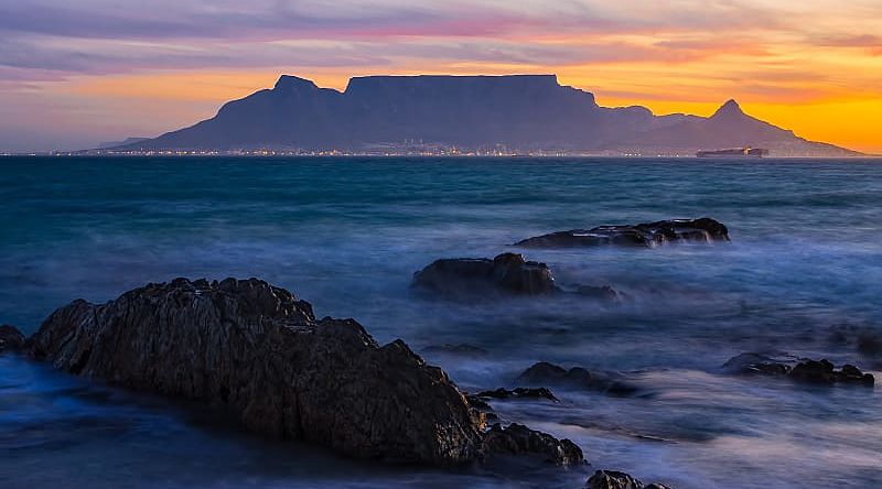 Silhouette of Table Mountain against sunset sky and ocean waves in Cape Town, South Africa
