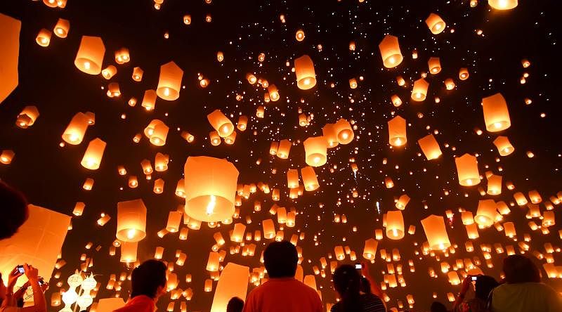Large group of people releasing lit lanterns into sky during floating lantern festival in Thailand