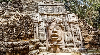 Ancient stone Mayan pre-columbian civilization pyramid with carved face in the forest, Lamanai archeological site, Orange Walk District, Belize