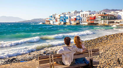 Romantic couple sitting on a beach bench near Little Venice in Mykonos, Greece