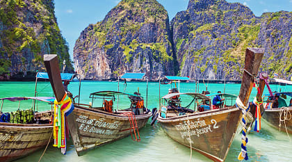 Wooden boats in the turquoise waters of Maya Bay with limestone karst cliffs on Phi Phi island in Thailand