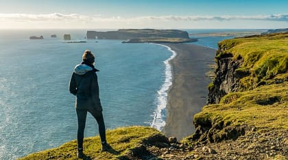 Hiker enjoying view of Reynisfjara black sand beach and Dyrholaey in the distance