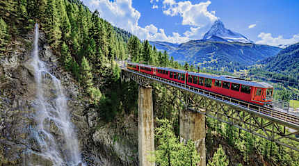 A red train crossing a high mountain bridge in Switzerland.