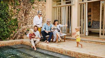 Smiling grandparents relaxing with children and grandchildren beside pool at villa during multigenerational family vacation