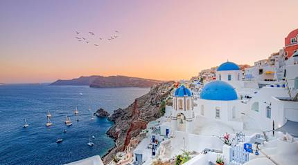 The sun sets over Oia’s blue-domed churches and Aegean Sea.