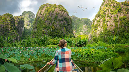 woman travels along river in boat, enjoying picturesque karst mountains in Ninh Binh Province, Vietnam