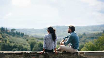 Couple sitting on stone wall overlooking rolling countryside hills in Tuscany, Italy