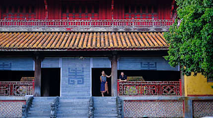 Travelers at the Imperial City of Hue, Vietnam, standing outside a historic temple with red columns and tiled roof.