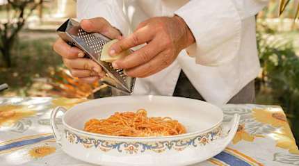 Chef grating Parmigiano cheese over a plate of pasta, Italy.