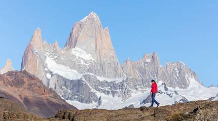 Hiker in red jacket walking with Mount Fitz Roy in Patagonia's stunning landscape as the backdrop