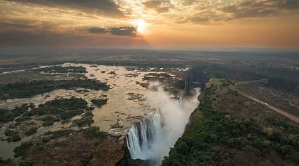 The mighty Victoria Falls cascades dramatically at sunset over Zambezi River.