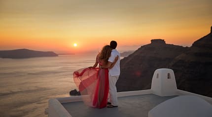 A couple watches the sunset over Santorini, Greece