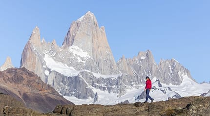 Hiker in red jacket walking with Mount Fitz Roy in Patagonia's stunning landscape as the backdrop