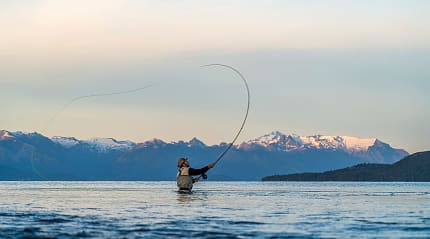 A fisherman casts gracefully in Río Negro’s waters, mountains towering behind.