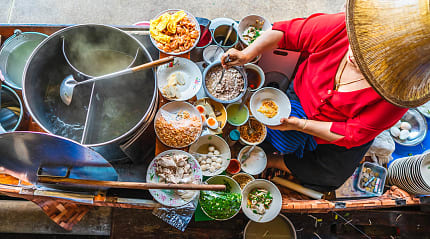 Woman preparing Thai noodle soup Tom Yum on boat in local floating market in Bangkok, Thailand
