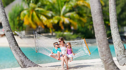 Mother swinging in a hammock on the beach with her kids in French Polynesia