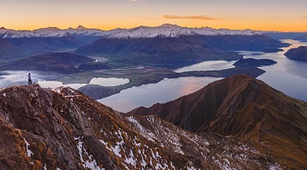 Hiker standing on a mountain trail, enjoying the beautiful sunrise over Lake Wanaka, New Zealand in winter