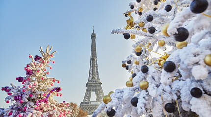 Snow-covered Christmas trees decorated with ornaments with the Eiffel Tower in the background, capturing the festive holiday in Paris, France
